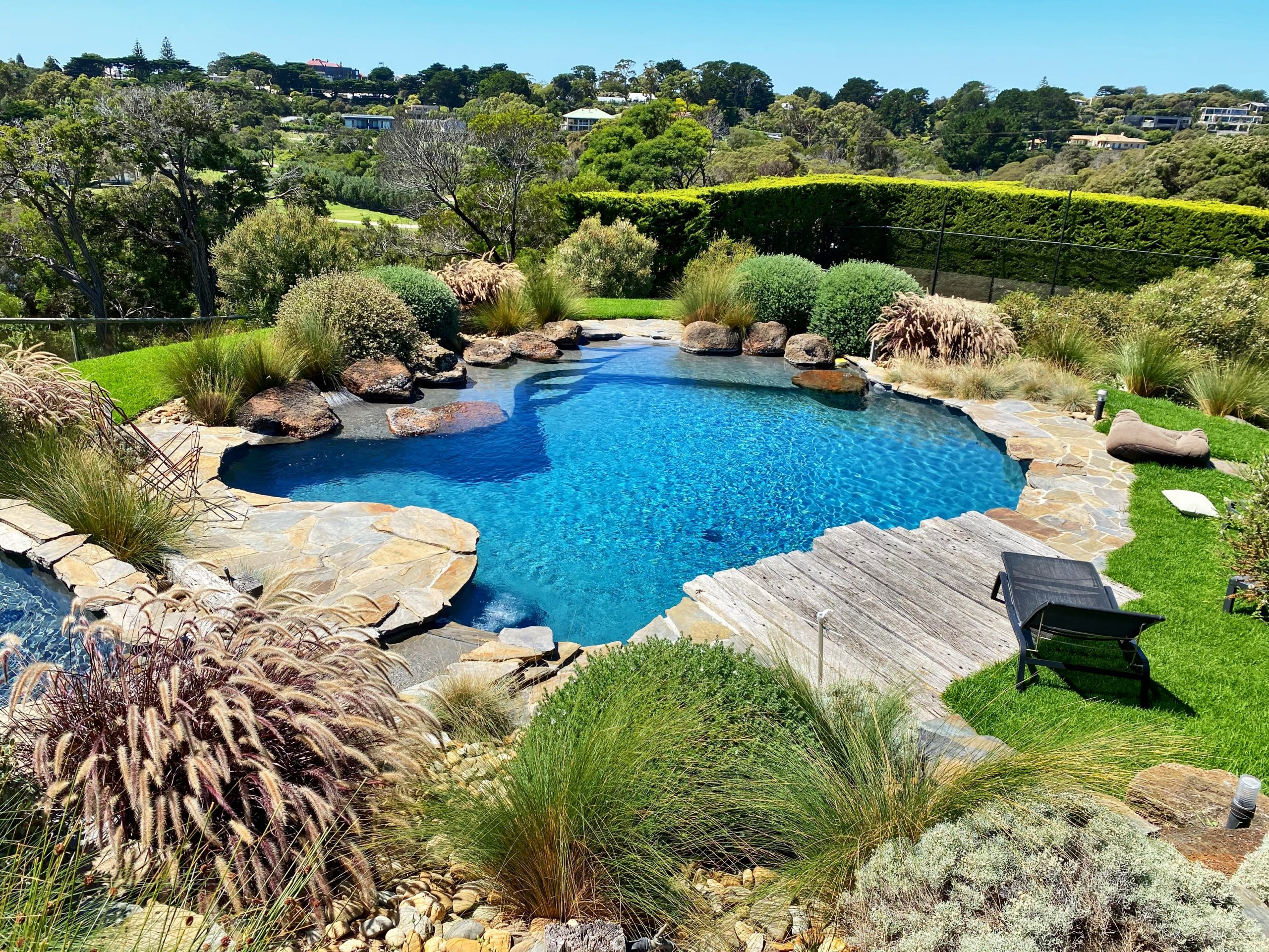 Gorgeous curved pool surrounded by stone paving and a wonderful garden — a true backyard oasis